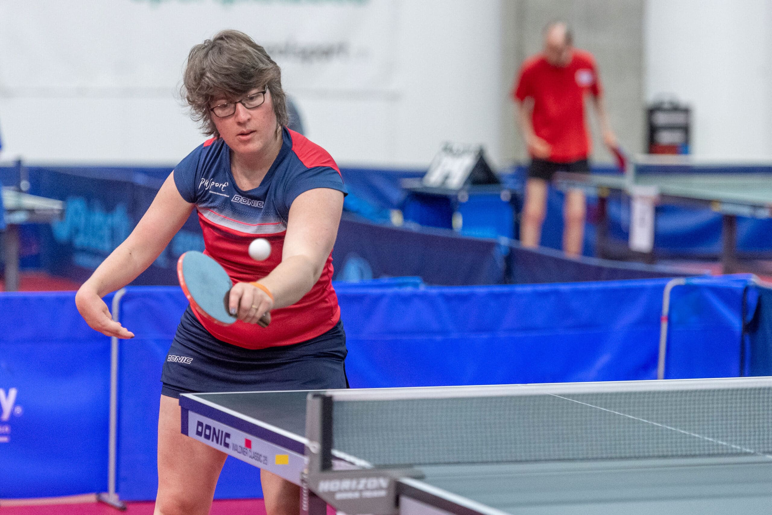 Tischtennisspielerin schlägt den Ball über den Tisch.