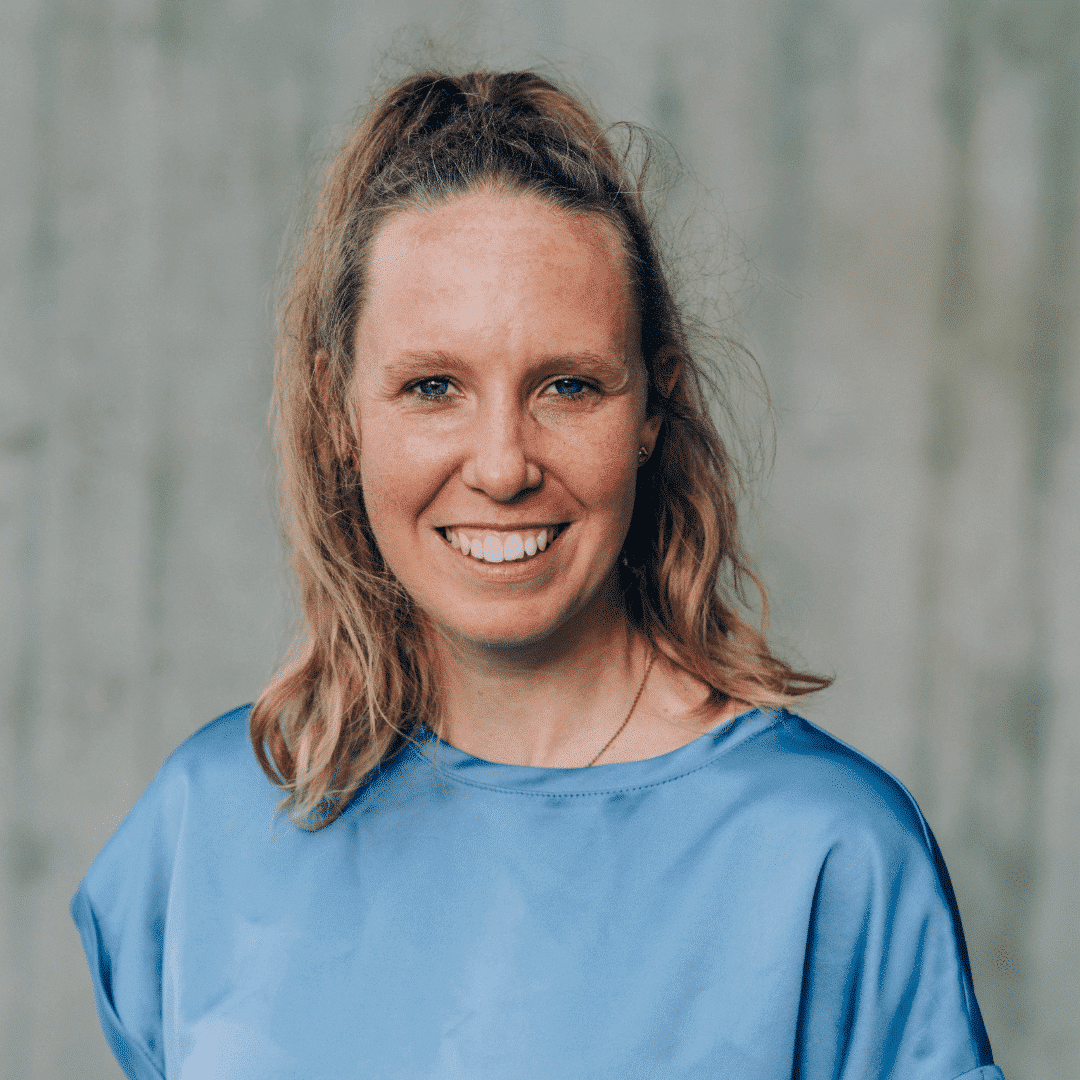 Lächelnde Person mit blauer Bluse vor Hintergrund.