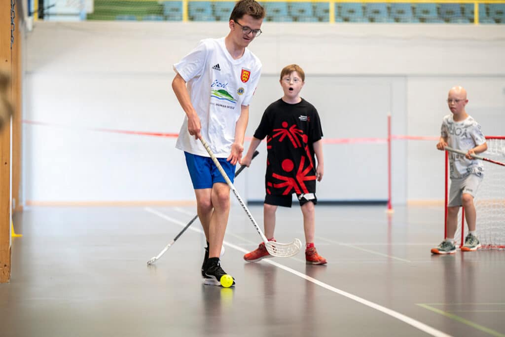 Kinder spielen Floorball in einer Sporthalle.