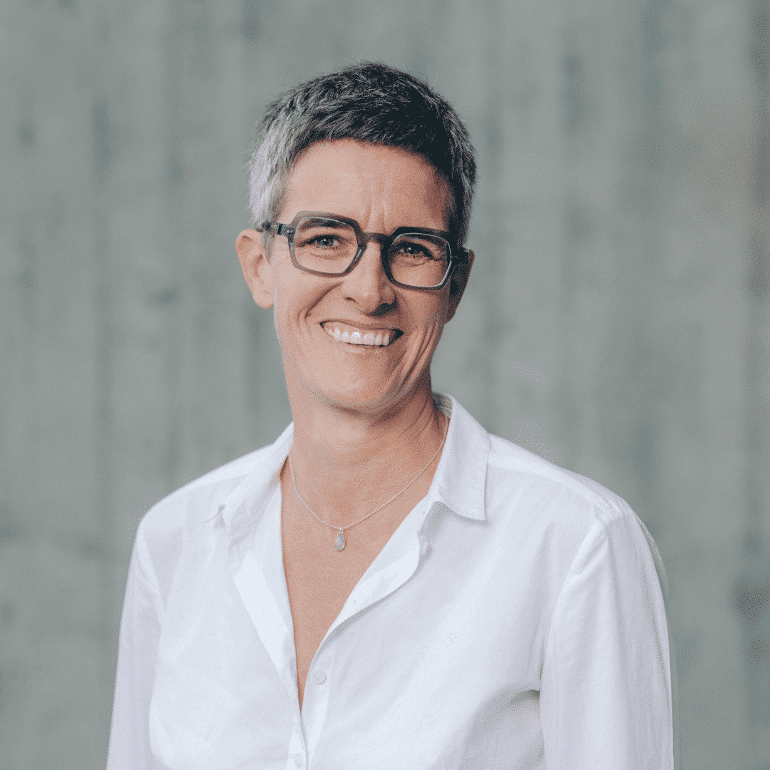 Lächelnde Person mit Brille und Kurzhaarfrisur.