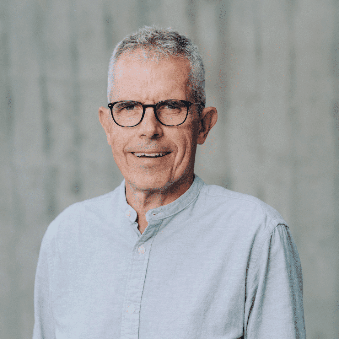 Lächelnder Mann mit Brille und hellblauem Hemd.