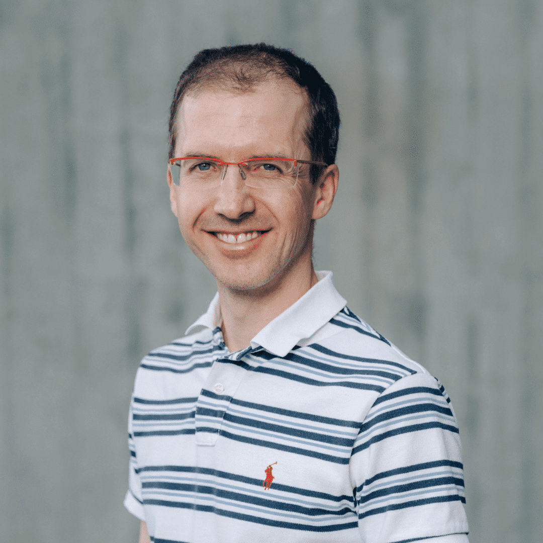 Lächelnder Mann mit Streifenhemd und Brille.