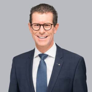 Mann mit Brille und Anzug lächelt freundlich.