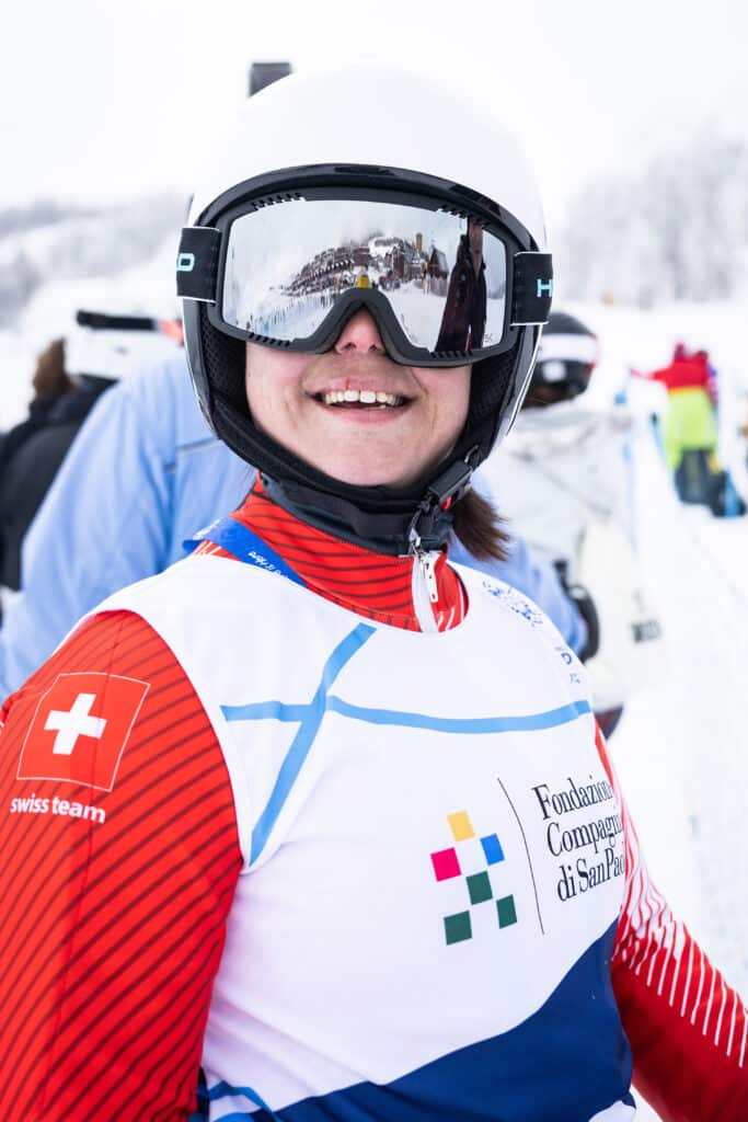 Smiling person in a ski outfit against a snowy background.