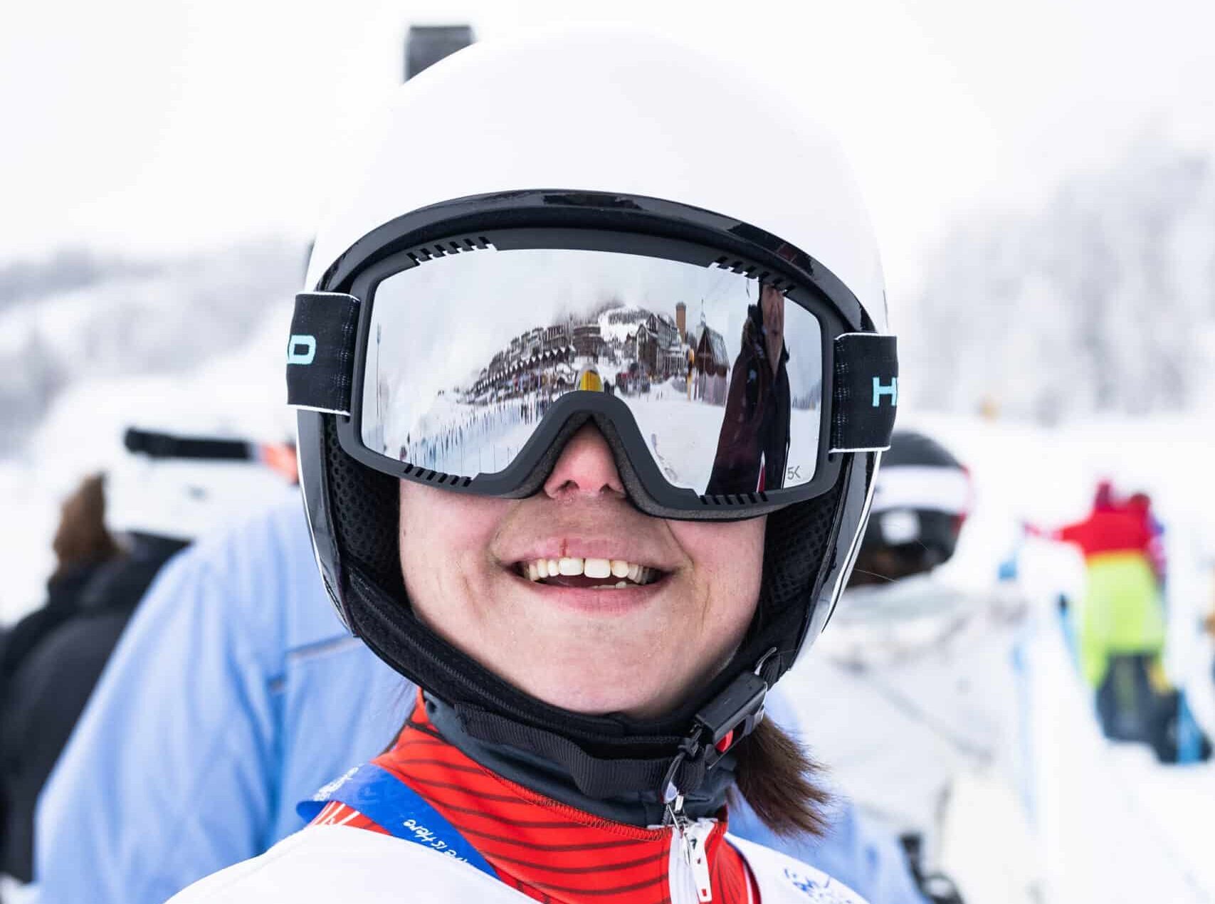 Persona sorridente in tenuta da sci su sfondo innevato.