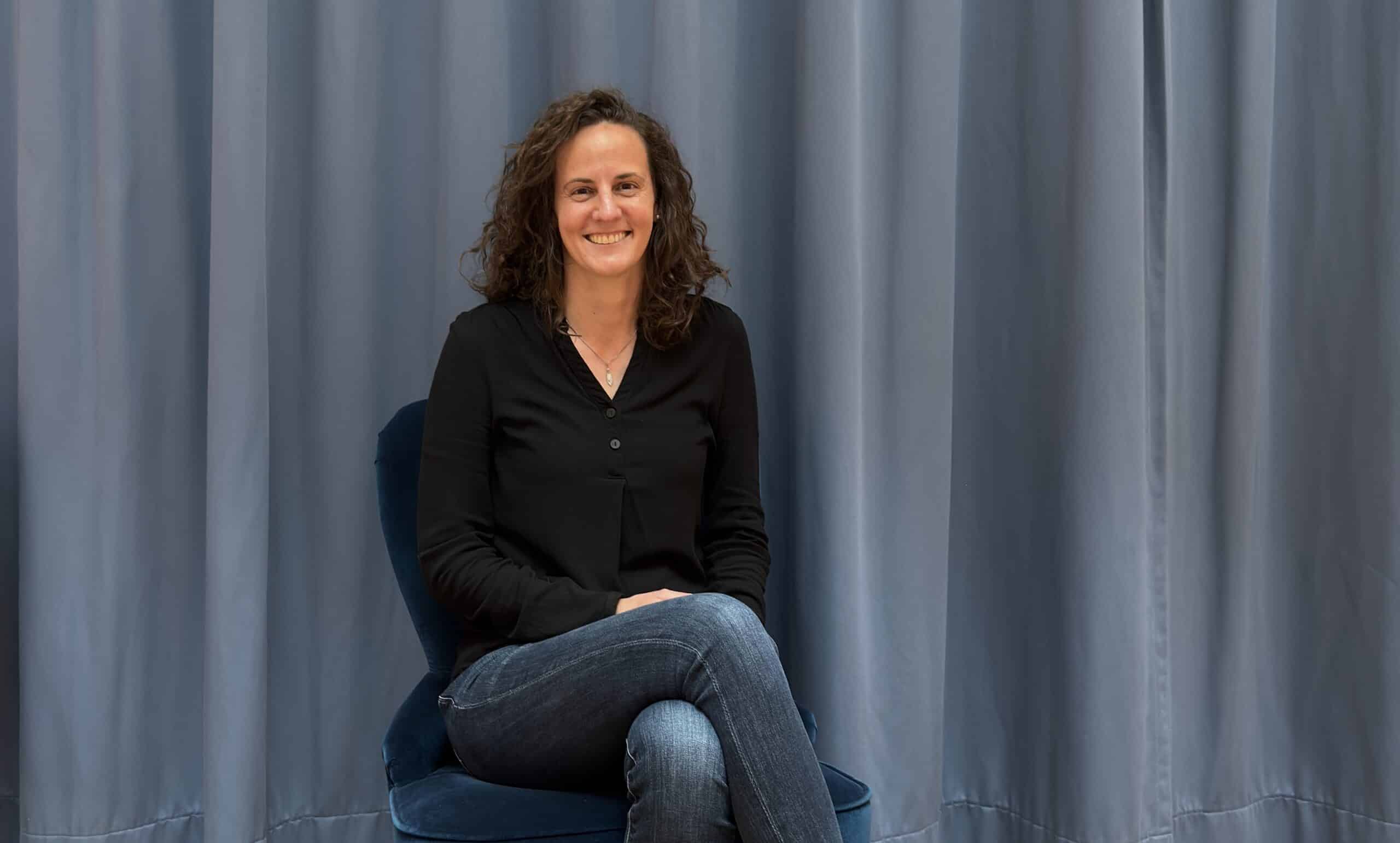 Lächelnde Frau sitzt vor blauen Vorhängen